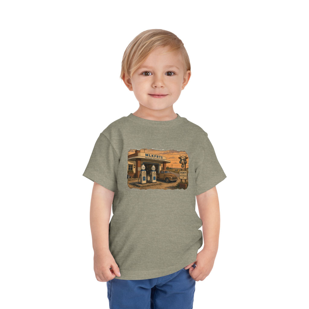 Toddler wearing the Peculiar Gas Station Toddler Tee in Heather Stone, gas station scene on the front