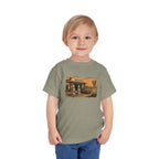 Toddler wearing the Peculiar Gas Station Toddler Tee in Heather Stone, gas station scene on the front