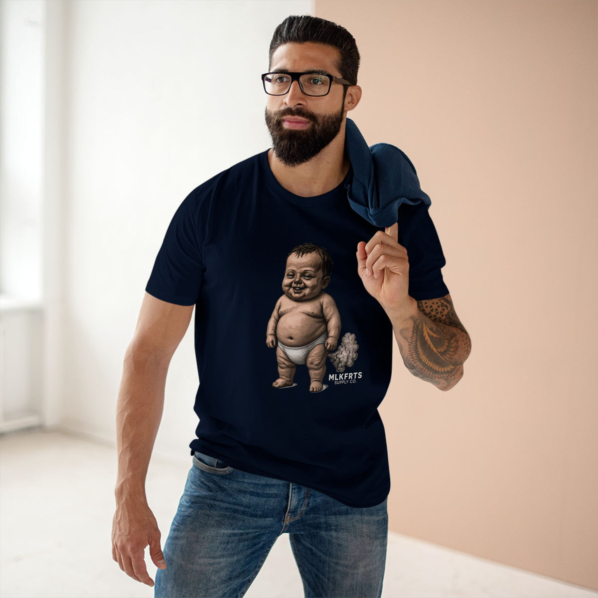 Man wearing the navy MLKFRTS Lil' Stinker Tee, smug diaper baby with gas cloud on the front