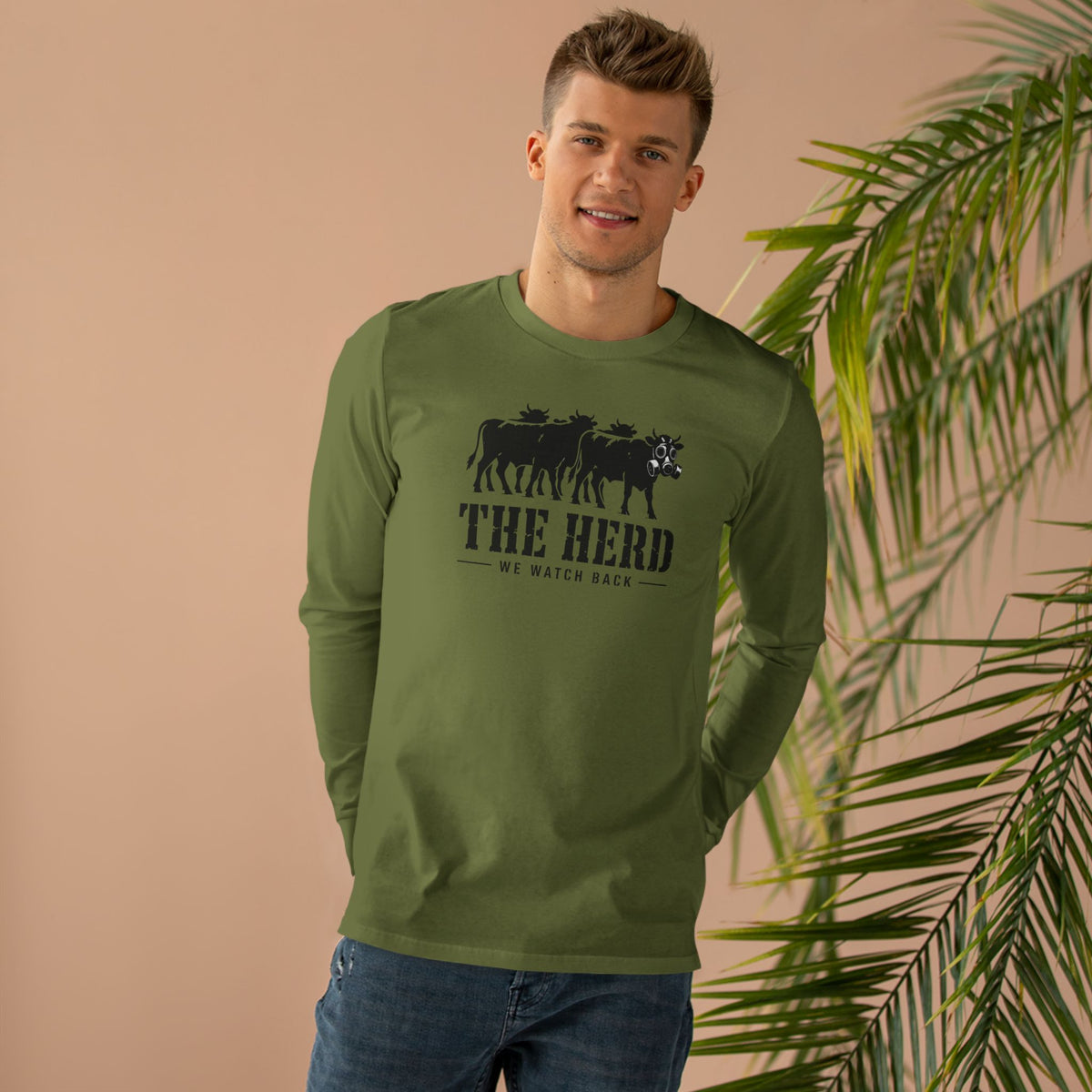 Man wearing the Watch Back Long Sleeve Tee in army green, front: cow lineup with one gas-mask cow, THE HERD, We Watch Back
