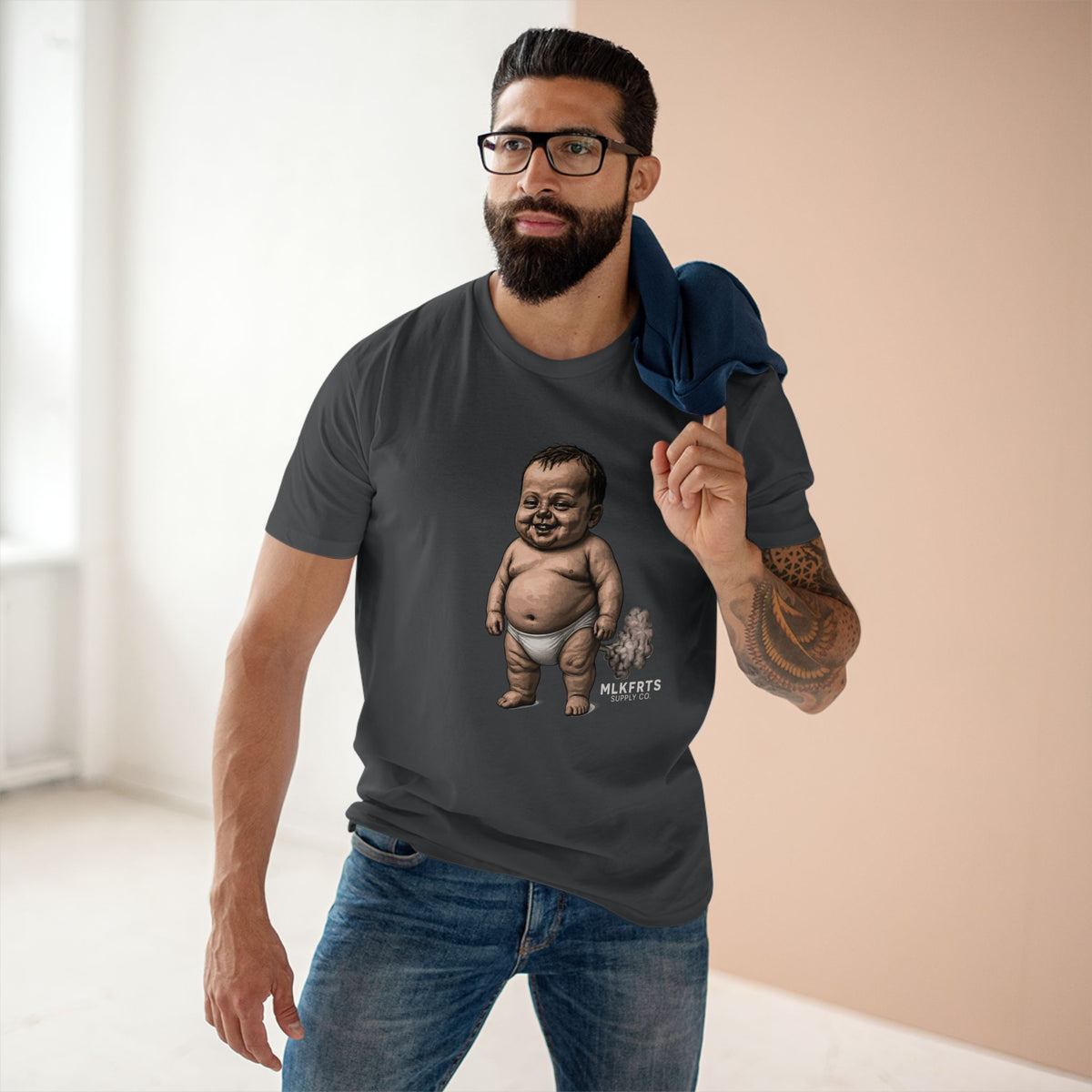 Man wearing the charcoal MLKFRTS Lil' Stinker Tee, smug diaper baby with gas cloud on the front