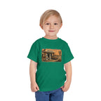 Toddler wearing the Peculiar Gas Station Toddler Tee in Kelly, gas station scene on the front