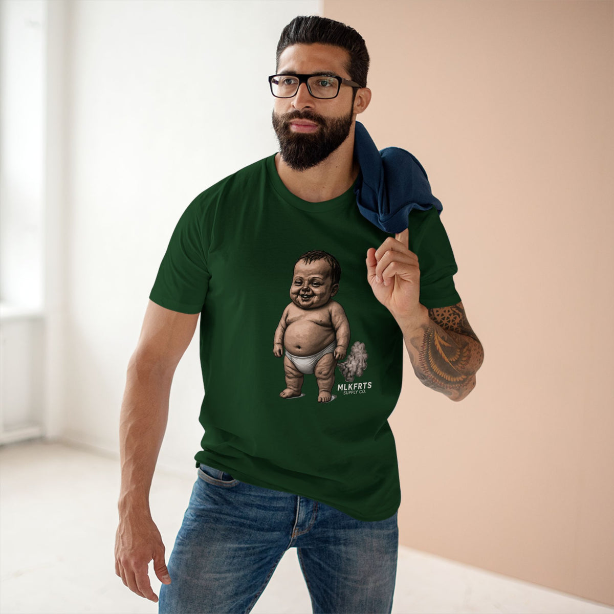 Man wearing the forest green MLKFRTS Lil' Stinker Tee, smug diaper baby with gas cloud on the front