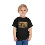 Toddler wearing the Peculiar Gas Station Toddler Tee in Black, gas station scene on the front
