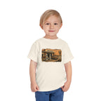 Toddler wearing the Peculiar Gas Station Toddler Tee in Natural, gas station scene on the front